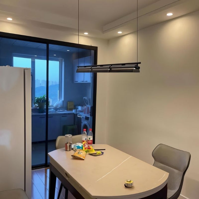 "Modern linear pendant light hanging above a dining table in a contemporary dining area with a sliding glass door."