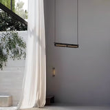 "Modern linear pendant light hanging near a window with sheer curtains, showing a minimalist interior."