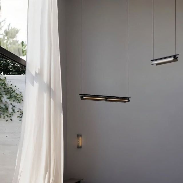 "Two modern linear pendant lights of different configurations hanging in a bright, minimalist space with a window."