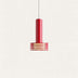 Red cylindrical pendant light with brass slotted shade hanging against a neutral background.