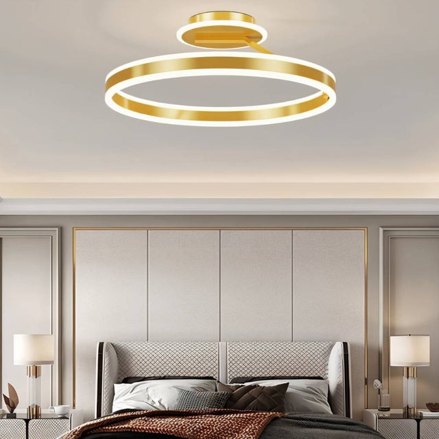 "A modern LED ceiling light with interlocking gold rings, illuminating a luxurious bedroom with a tufted headboard and matching nightstands."