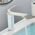 White and gold modern bathroom faucet displayed on a sink with running water and toiletries in background.