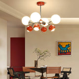 "A multi-light mid-century modern chandelier with red and white acrylic globe diffusers, hanging above a dining table in a modern dining room with artwork."