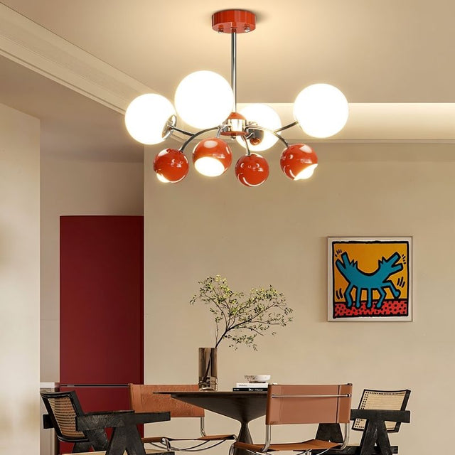 "A multi-light mid-century modern chandelier with red and white acrylic globe diffusers, hanging above a dining table in a modern dining room with artwork."