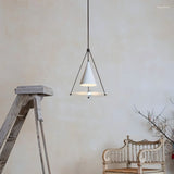 "A modern white pendant light with a cone shade and frosted glass disc in a room with a ladder and chair."