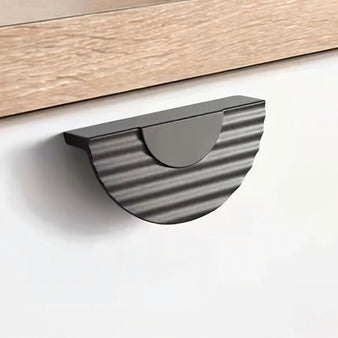 "Black semi-circular drawer pull with ridged texture mounted on a modern cabinet."