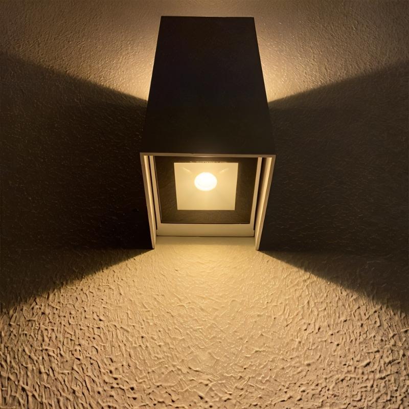 "A minimalist rectangular aluminum outdoor wall lamp with a glass diffuser, casting light on a textured wall."
