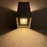 "A minimalist rectangular aluminum outdoor wall lamp with a glass diffuser, casting light on a textured wall."