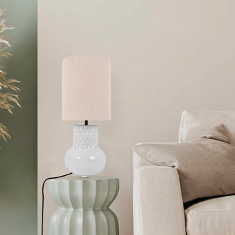 "A modern ceramic table lamp with a textured base and a light-colored shade sits on a side table in a living room setting."