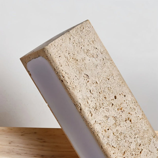 "Close-up detail of a modern wall lamp with an angled yellow travertine shade, showcasing the texture of the stone and the soft light it emits."