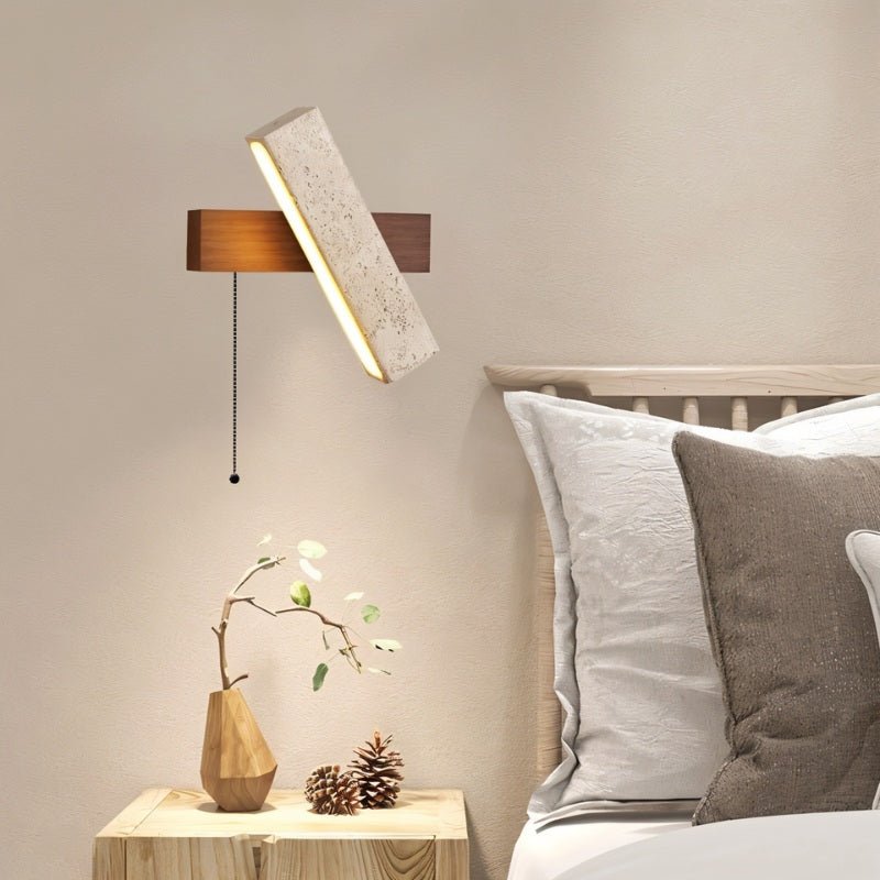 "A modern wall lamp with an angled yellow travertine shade and a walnut rectangular base, mounted on a wall above a wooden nightstand in a bedroom, casting a warm, ambient light."