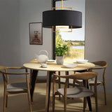 "A black pendant light with a gold frame hanging over a dining table with a view of a lake."