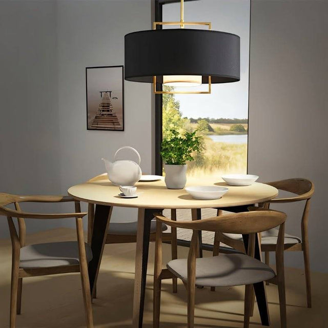 "A black pendant light with a gold frame hanging over a dining table with a view of a lake."