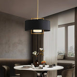 "A black pendant light with a gold frame hanging over a dining table."