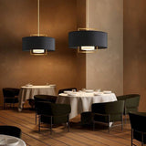 "Two black pendant lights with gold frames hanging over dining tables in a restaurant setting."