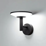 "A modern, circular outdoor wall lamp casting a bright light on a gray wall at night."
