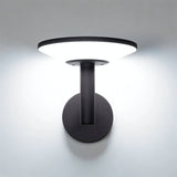 "A modern, circular outdoor wall lamp illuminating a white wall with a soft, diffused light."