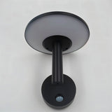 "A modern, circular outdoor wall lamp with a motion sensor, mounted on a light gray wall."