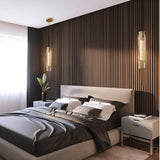 "Pair of elegant pendant lights with elongated, faceted crystal shades and brass frames flanking a modern bed, serving as both pendant lights and wall sconces."