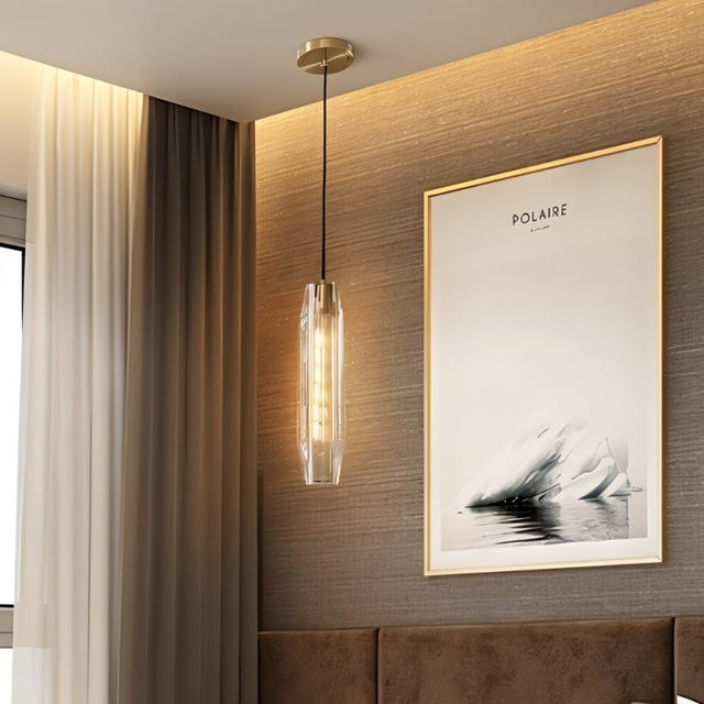 "Refined pendant light with an elongated, faceted crystal shade and brass frame casting a captivating glow in a modern bedroom setting."
