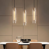 "Elegant pendant lights with elongated, faceted crystal shades and brass frames hanging above a modern dining table, creating a captivating glow."