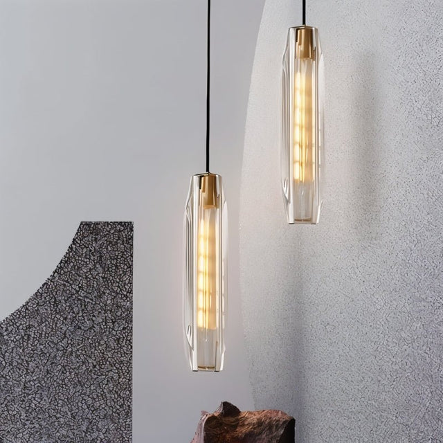 "Pair of refined pendant lights with elongated, faceted crystal shades and brass frames, creating a captivating glow in a modern space with artistic wall features."
