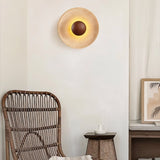 "A modern, circular wall lamp made of yellow travertine with a walnut wood center, mounted on a wall in a living room, casting a warm, ambient glow."
