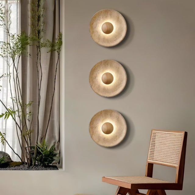"Three modern, circular wall lamps made of yellow travertine with walnut wood centers, arranged vertically on a wall, providing a warm, ambient glow in a contemporary space."