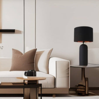 "A modern ceramic table lamp with a black shade illuminates a contemporary living room with a white sofa."