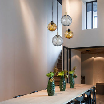 "Four modern pendant lights with spherical glass shades and intricate patterns, hanging above a long dining table in a contemporary setting."