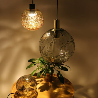 "Modern pendant lights with spherical glass shades and intricate patterns, hanging above a round wooden table with a potted plant."