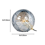 "A modern table lamp with a spherical patterned glass shade and metal-acrylic details, providing a soft, diffused light."