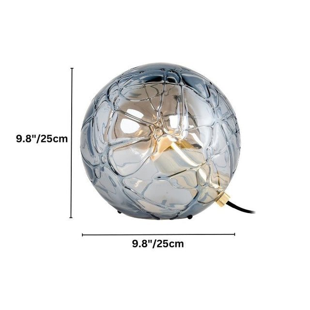 "A modern table lamp with a spherical patterned glass shade and metal-acrylic details, providing a soft, diffused light."