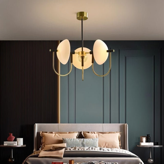 "Modern gold three-light chandelier with frosted glass orbs hanging over a bed in a bedroom."