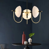 "Modern gold three-light chandelier with frosted glass orbs hanging over a table against a dark wall."