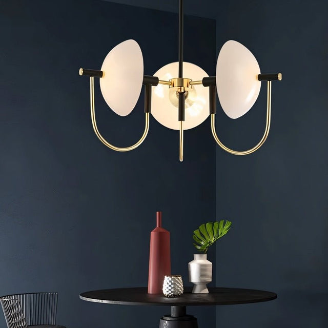 "Modern gold three-light chandelier with frosted glass orbs hanging over a table against a dark wall."