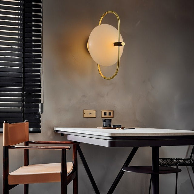 "Brass wall lamp with a frosted glass globe in a modern dining room, providing a warm, ambient glow."