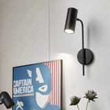 "A minimalist industrial black bedside reading lamp with a cylindrical shade and adjustable arm, mounted on a white wall next to a framed Captain America poster."