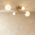 Gold mid-century modern ceiling light with six frosted white globe shades on dark wall with curtains and artwork.