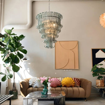 "A tiered glass chandelier hanging in a living room with a couch and artwork."