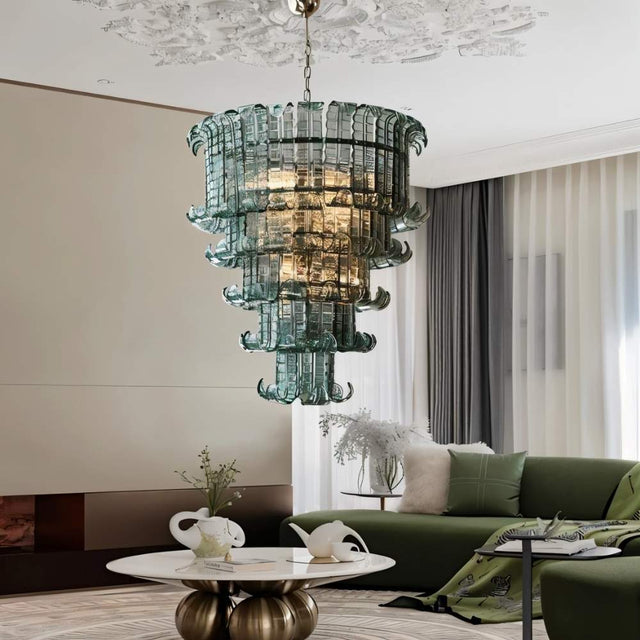 "A tiered glass chandelier hanging in a living room with a couch and artwork."