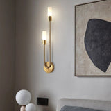 "A modern brass wall lamp with two acrylic diffusers illuminating a bedroom with artwork."
