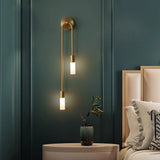 "A modern brass wall lamp with two acrylic diffusers illuminating a bedroom nightstand."