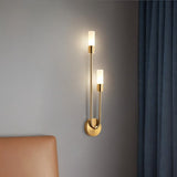 "A modern brass wall lamp with two acrylic diffusers illuminating a bedroom wall."