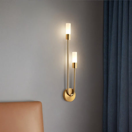 "A modern brass wall lamp with two acrylic diffusers illuminating a bedroom wall."