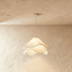 Layered petal pendant light with cream fabric shades hanging in white studio setting above table with magazine.