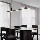 "Linear pendant light with red and black accents over a dining table with black chairs."