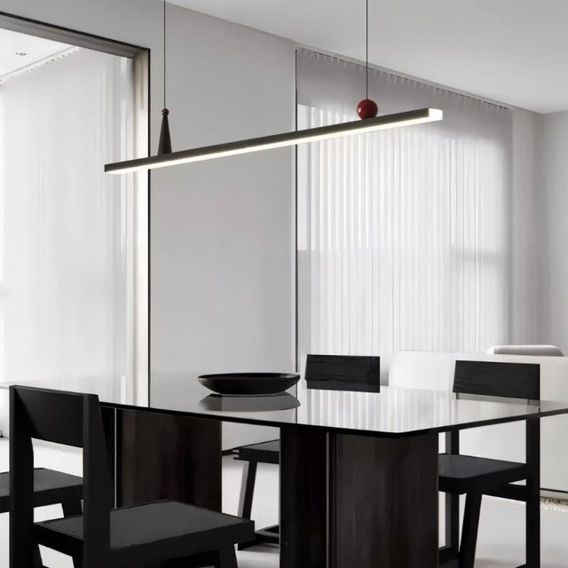 "Linear pendant light with red and black accents over a dining table with black chairs."