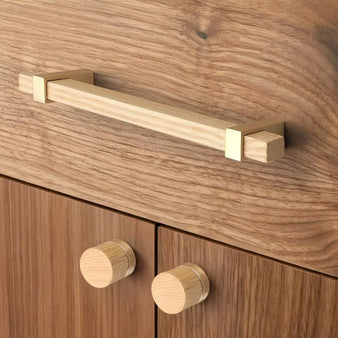 "Modern light wood pull bar and matching knobs with gold metallic brackets on a contemporary cabinet."