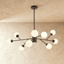 Gold mid-century modern chandelier with twelve frosted white glass globes in lifestyle setting above beige sofa against blue